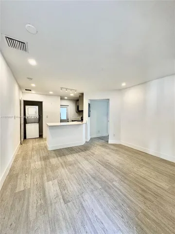 a view of empty room with wooden floor and kitchen