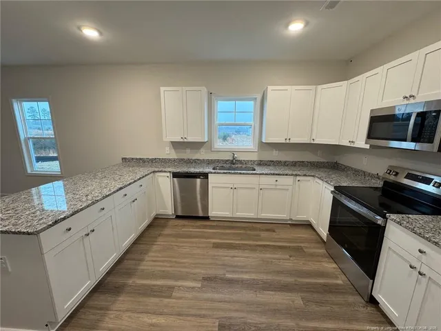 a large white kitchen with granite countertop a stove top oven a sink dishwasher and white cabinets with wooden floor