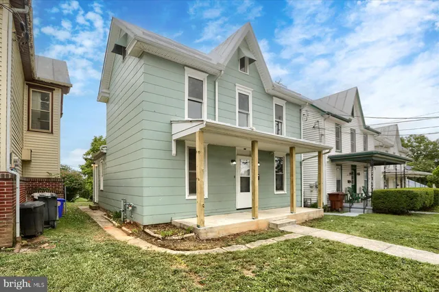 a view of a white house with large windows and table and chairs in a yard