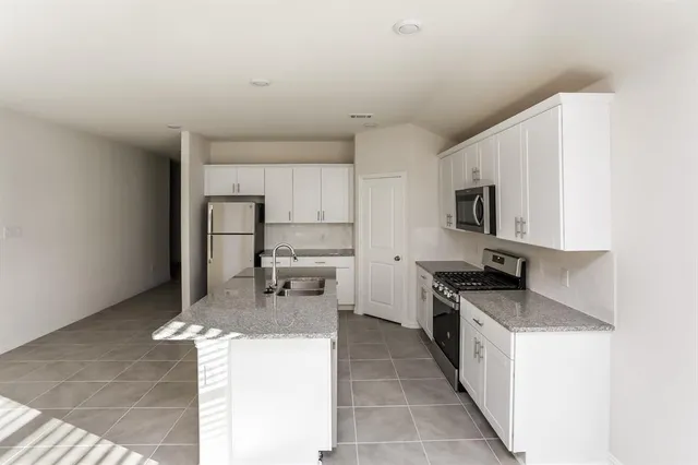 a kitchen with stainless steel appliances granite countertop a stove top oven a sink a refrigerator and white cabinets with wooden floor