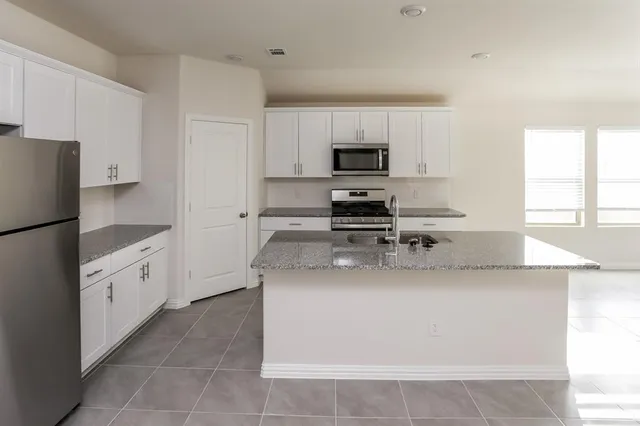 a large kitchen with stainless steel appliances a sink a stove a microwave a refrigerator and cabinets