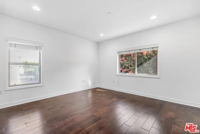 a view of an empty room with wooden floor and a ceiling fan