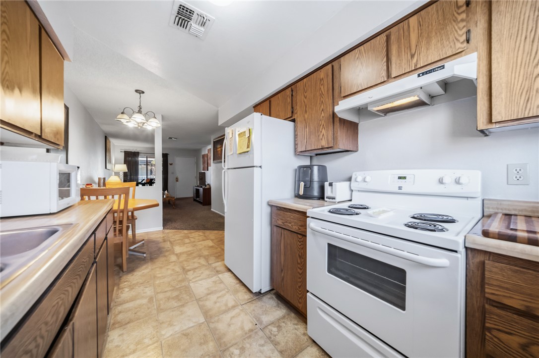793 Baseline Road Bullhead City, AZ 86442 - Photo 20 of 49 Functional kitchen featuring wood cabinetry, laminate countertops, a white electric range with a coordinating range hood, and tile flooring