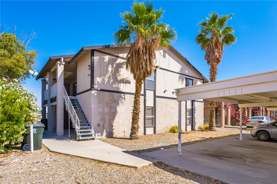 793 Baseline Road Bullhead City, AZ 86442 - Photo 4 of 49 Two-story multifamily building with a stucco exterior, featuring covered parking, mature palm trees, and exterior stair access to upper units
