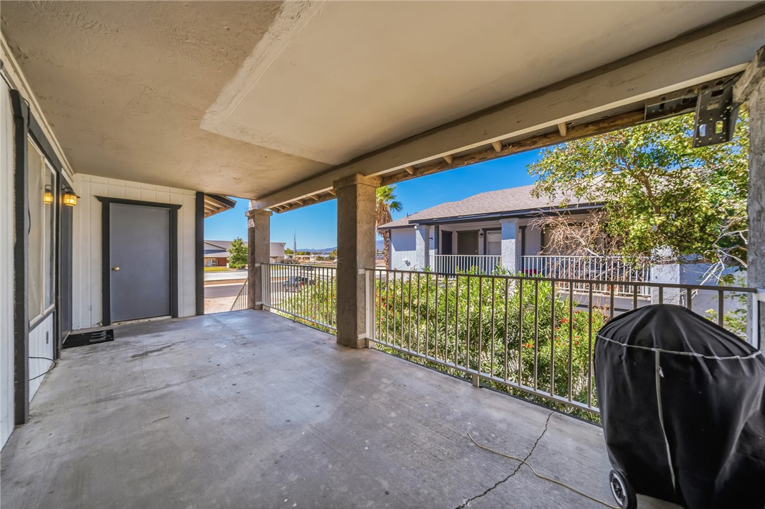 793 Baseline Road Bullhead City, AZ 86442 - Photo 10 of 49 Covered concrete patio space featuring a dark gray door with white trim, wall-mounted exterior lighting, and a metal railing