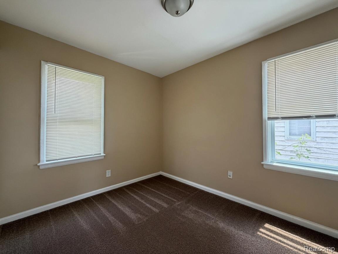 7286 Faust Avenue Detroit, MI 48228 - Photo 11 of 19 Room featuring neutral-toned walls, brown carpet, two windows with blinds, white trim, and a ceiling-mounted light fixture