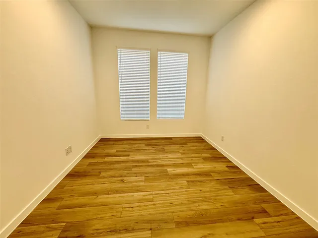 a view of an empty room with wooden floor kitchen view and a window