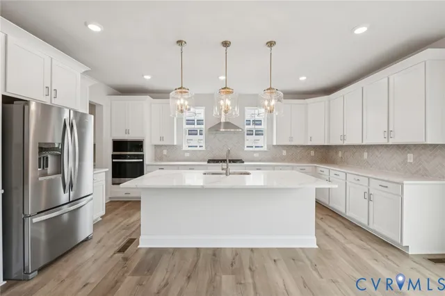a large kitchen with stainless steel appliances kitchen island granite countertop a refrigerator a sink dishwasher a stove and a dining table with wooden floor