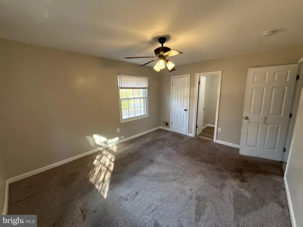an empty room with chandelier fan and windows