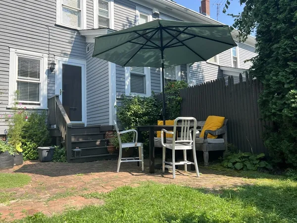a backyard of a house with table and chairs under an umbrella