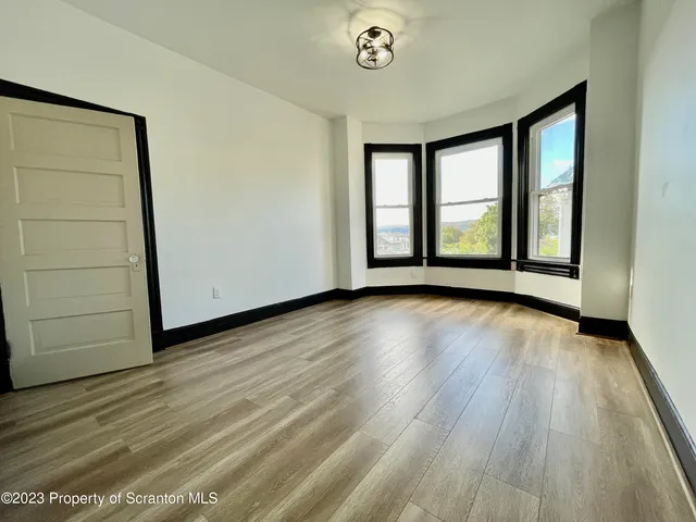 a view of an empty room with window and hardwood floor