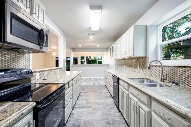 a large kitchen with granite countertop a stove top oven a sink a window and wooden cabinets