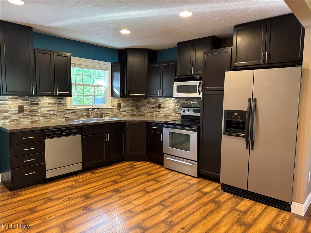 Kitchen featuring refrigerator with ice dispenser, dishwasher, electric range, microwave, and sink.