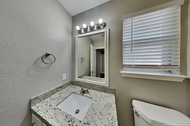 a bathroom with a granite countertop sink a toilet and mirror