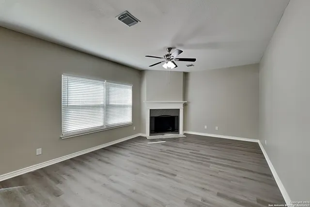 a view of an empty room with wooden floor fireplace and a window