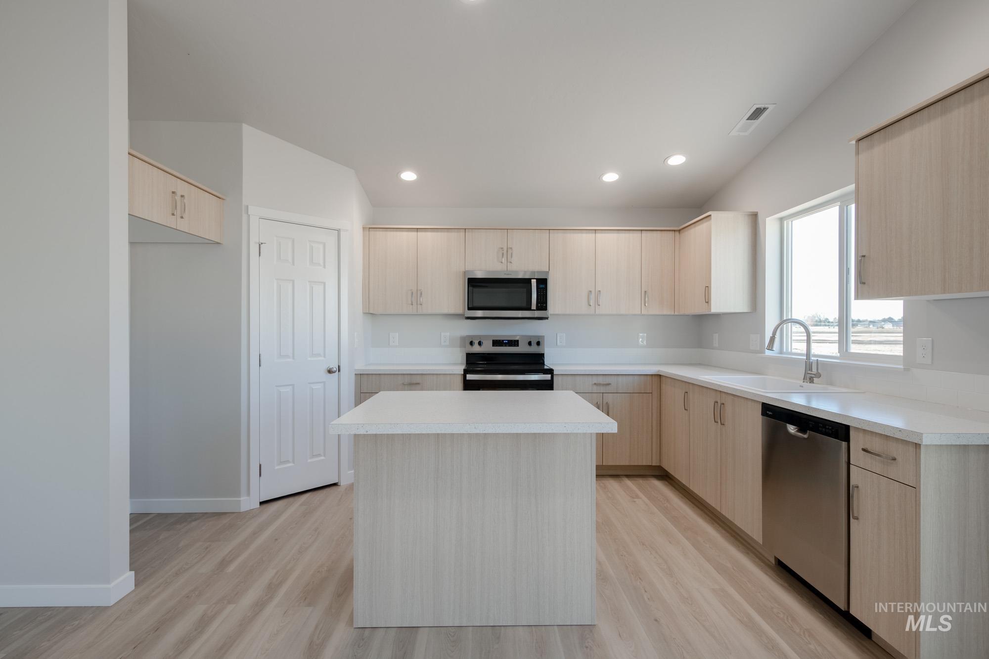 7472 South Menzingers Avenue Meridian, ID 83642 - Photo 4 of 22 Kitchen with light brown cabinetry, appliances with stainless steel finishes, a center island, light countertops, and light wood-type flooring