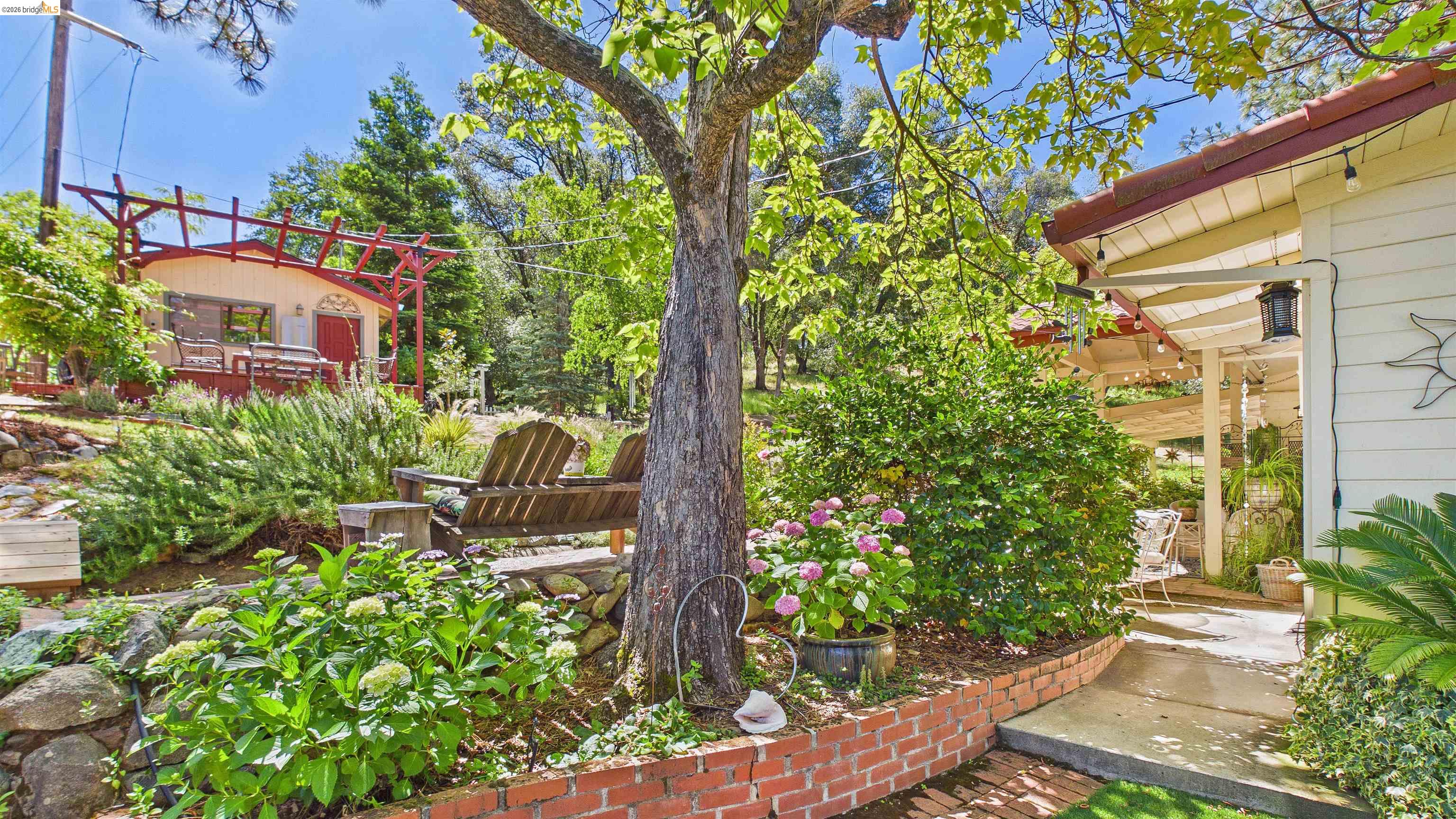 18102 Mt Eaton Road Tuolumne, CA 95379 - Photo 29 of 44 Terraced landscape featuring mature trees, diverse plantings, brick garden beds, and stone retaining walls