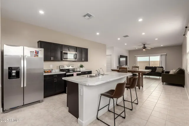 a kitchen with stainless steel appliances granite countertop a refrigerator a sink a stove a dining table and chairs