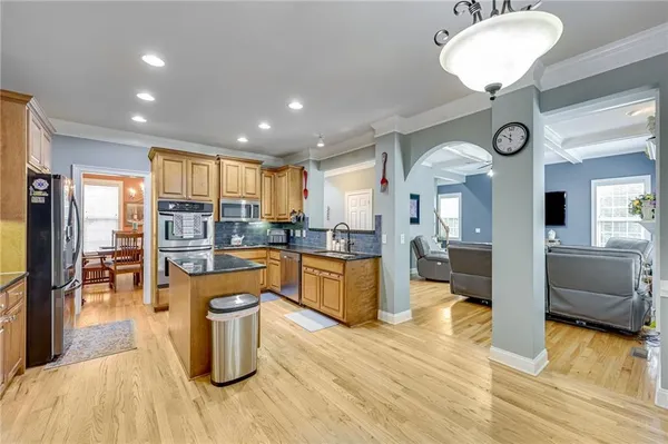 a kitchen with stainless steel appliances granite countertop a refrigerator a sink dishwasher a stove and a dining table with wooden floor