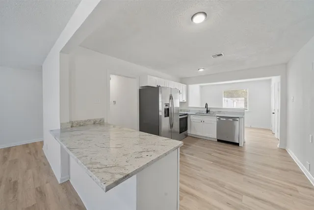 a kitchen with stainless steel appliances granite countertop a sink dishwasher a refrigerator and white cabinets with wooden floor