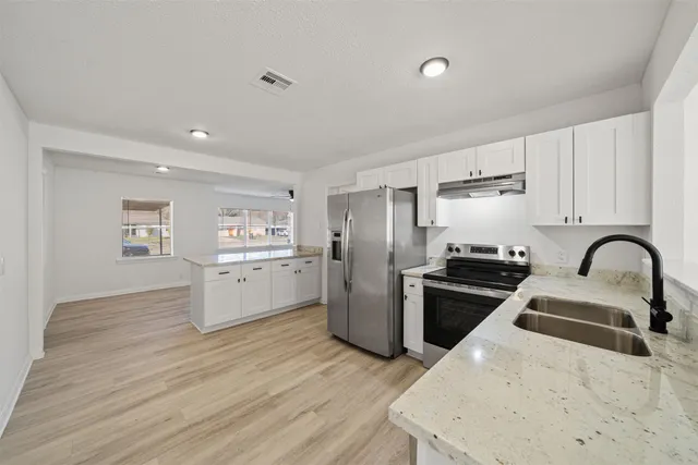 a kitchen with refrigerator a stove a sink and white cabinets with wooden floor