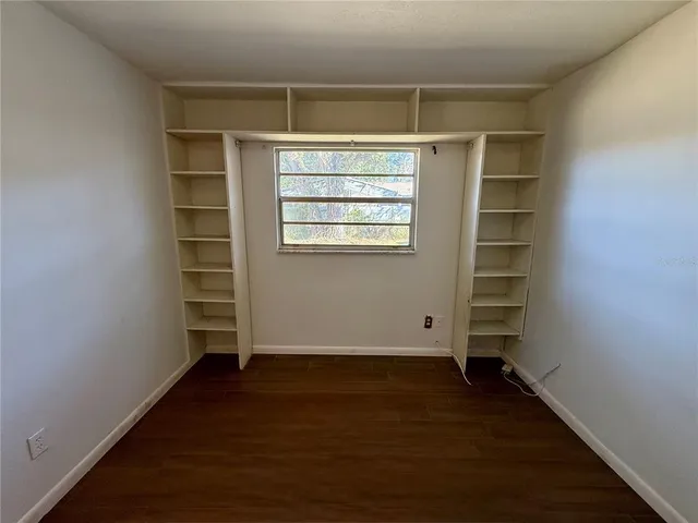 an empty room with wooden floor closet and windows