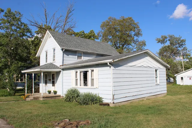 a view of a white house next to a yard with plants and trees