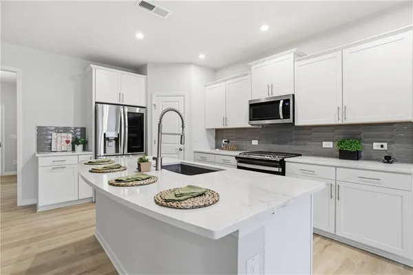 a kitchen with stainless steel appliances kitchen island granite countertop a stove a sink a refrigerator a white table and white cabinets