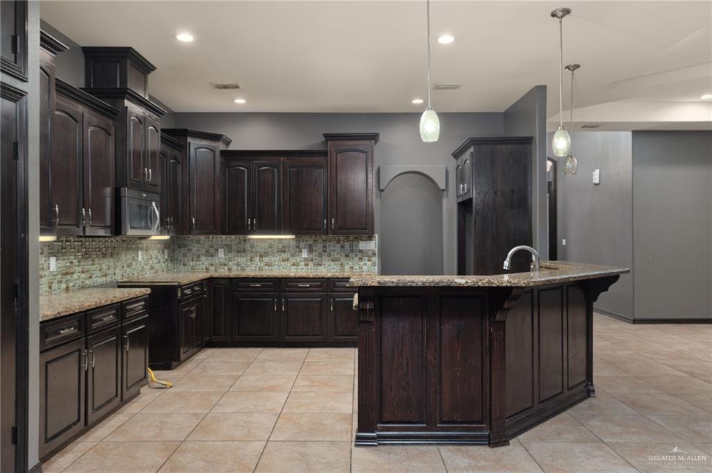 401 Ric Mar Street Edinburg, TX 78541 - Photo 6 of 18 Kitchen featuring extensive dark wood cabinetry, granite countertops, an undermount sink with a gooseneck faucet, a mosaic tile backsplash, and recessed lighting