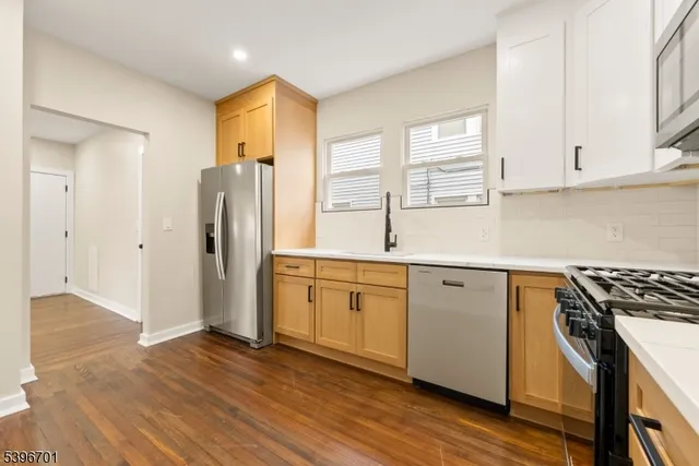 a kitchen with stainless steel appliances granite countertop a refrigerator a sink and white cabinets with wooden floor