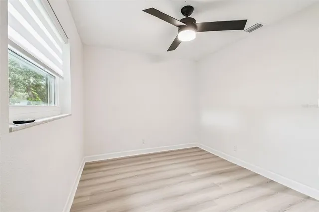an empty room with wooden floor ceiling fan and windows