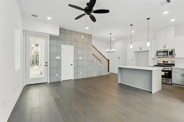 a view of an empty room and kitchen with wooden floor