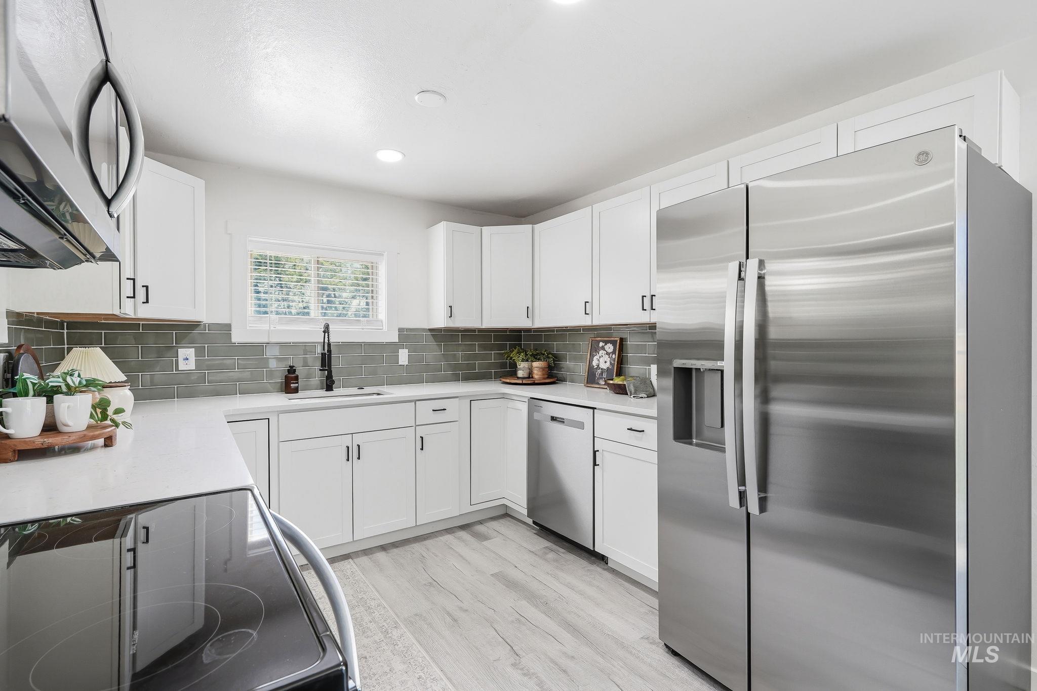 2152 Artesian Road Eagle, ID 83616 - Photo 17 of 50 Contemporary kitchen featuring white cabinetry, light countertops, a sleek subway tile backsplash, stainless steel appliances, and wood-finish flooring