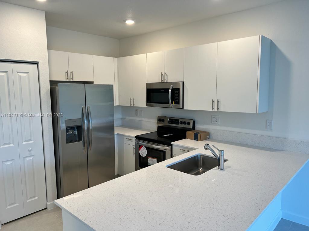 2633 Southeast 10th Street, Unit 2633 Homestead, FL 33035 - Photo 7 of 42 a kitchen with a refrigerator a sink a stove a microwave and wooden cabinets