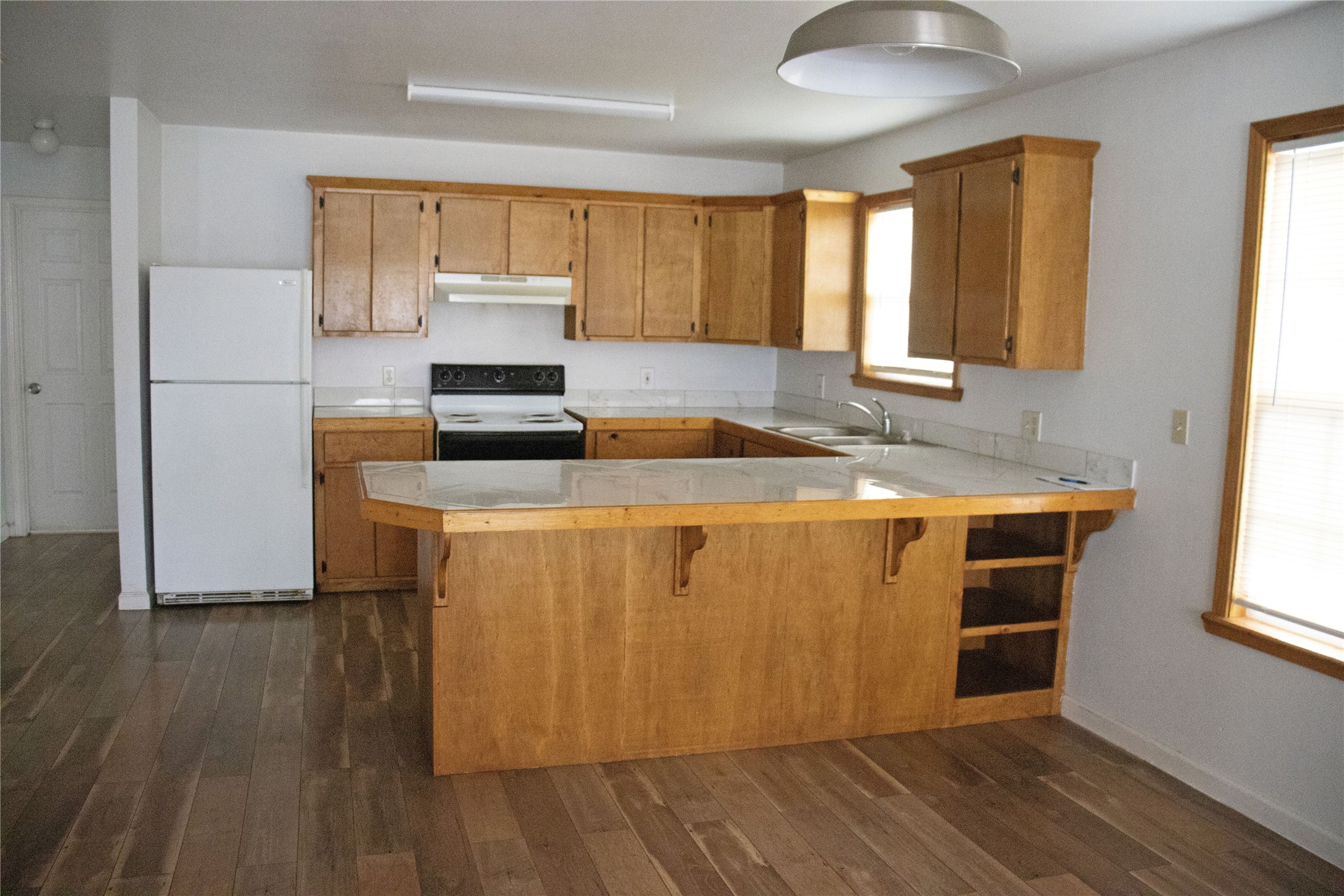 633 South Commerce Street Lockhart, TX 78644 - Photo 12 of 29 Kitchen featuring wood-finish flooring, light wood cabinetry, white countertops with a tile backsplash, and a built-in breakfast bar