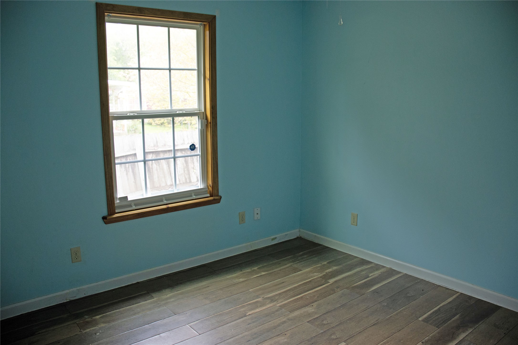 633 South Commerce Street Lockhart, TX 78644 - Photo 13 of 29 Room featuring wood-finish flooring, light blue walls, white baseboards, and a window with wood trim