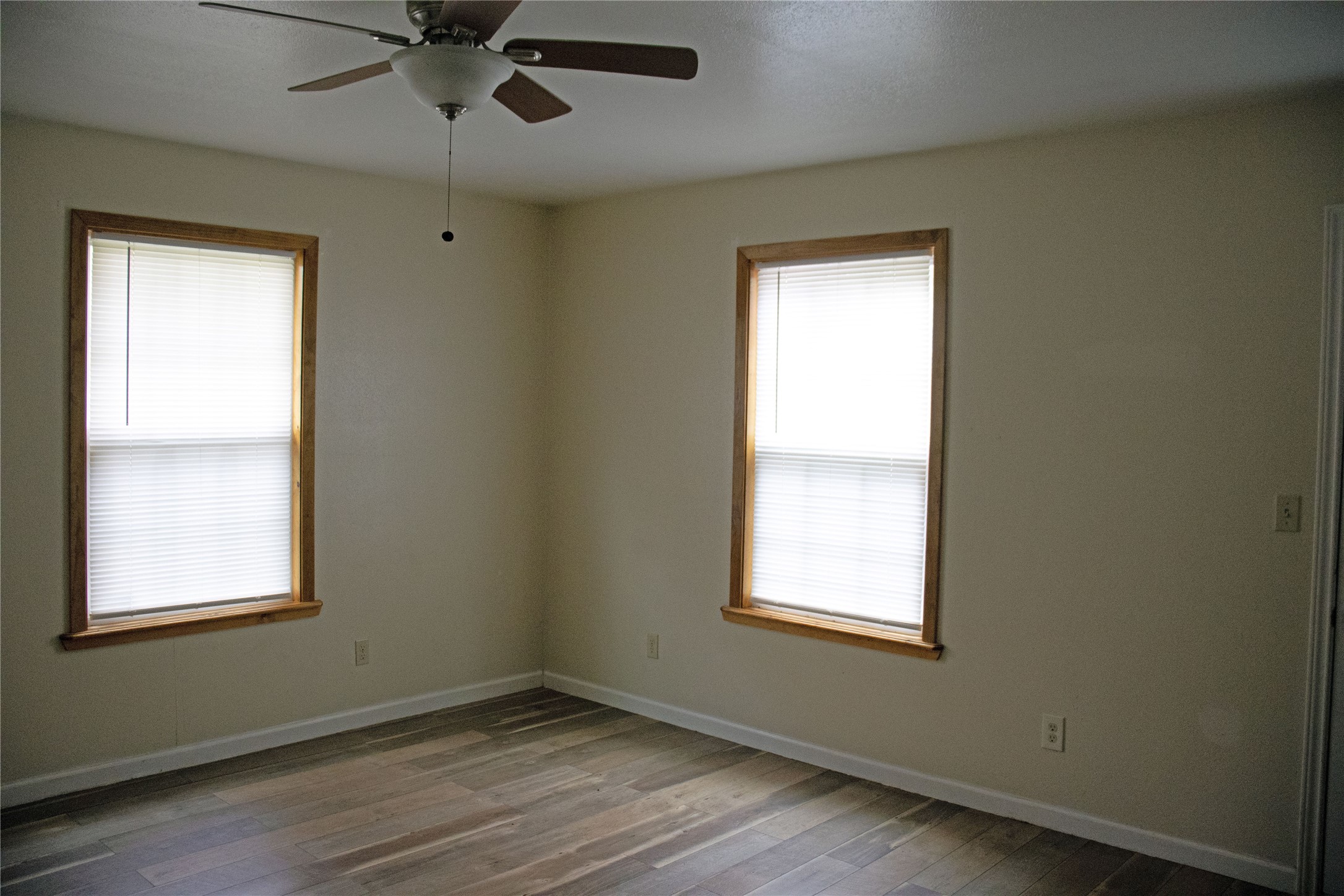 633 South Commerce Street Lockhart, TX 78644 - Photo 15 of 29 Spacious interior featuring wood-finish flooring, two windows with wood trim and blinds, and a ceiling fan with integrated lighting