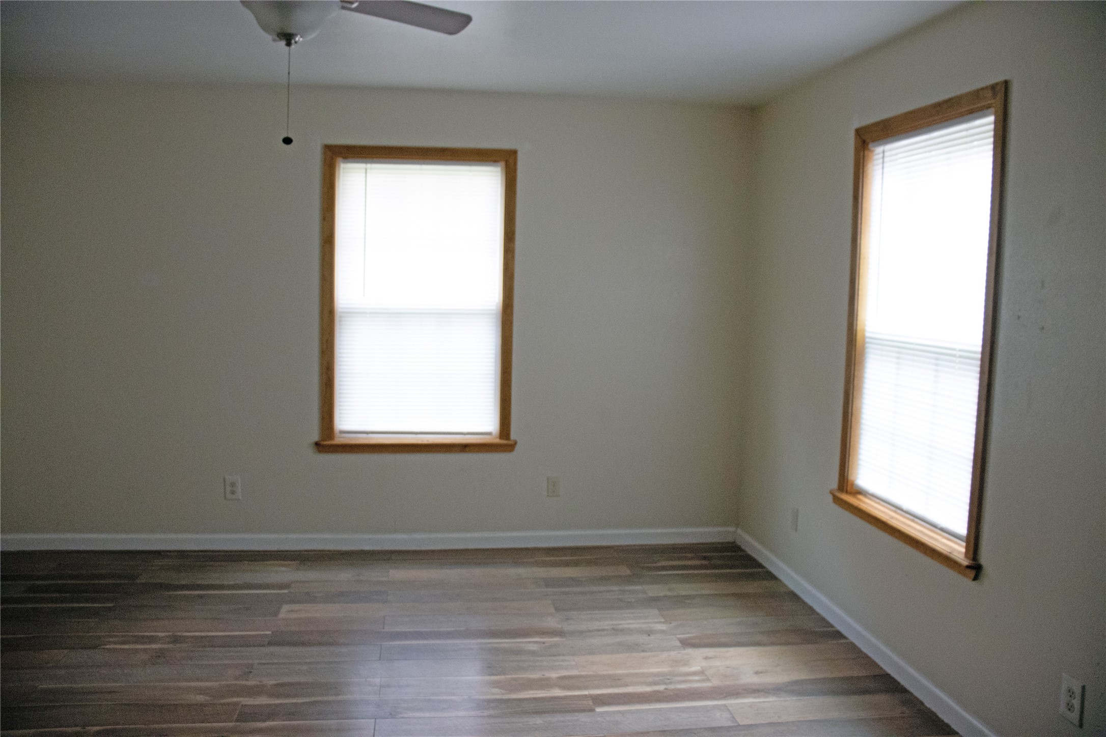 633 South Commerce Street Lockhart, TX 78644 - Photo 18 of 29 Spacious room featuring wood-finish flooring, two windows with wood trim, and a ceiling fan