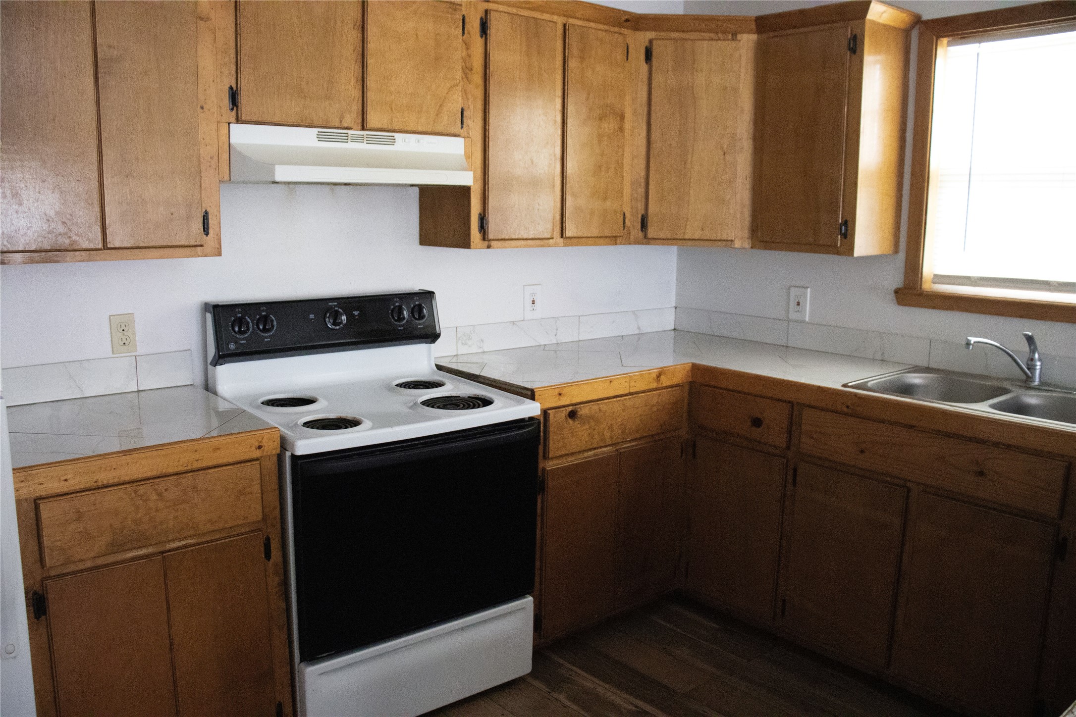 633 South Commerce Street Lockhart, TX 78644 - Photo 27 of 29 Kitchen featuring wood-finish cabinetry, white countertops, tile backsplash, double basin stainless steel sink, and a four-burner electric range with an overhead vent