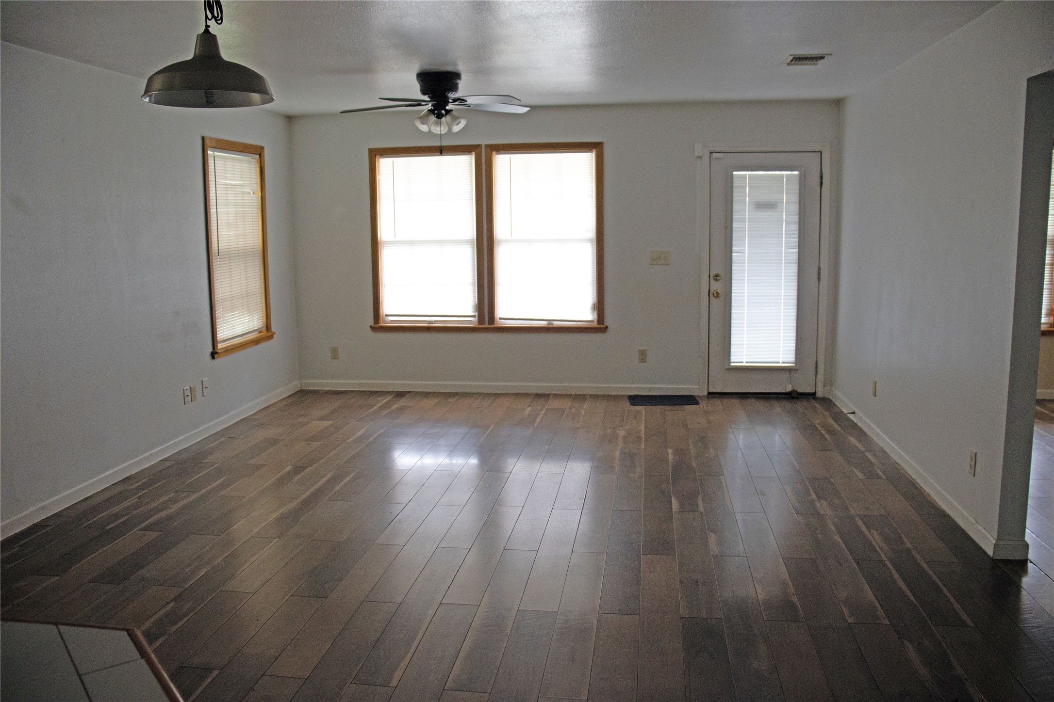 633 South Commerce Street Lockhart, TX 78644 - Photo 3 of 29 Spacious room featuring wood-finish flooring, multiple windows with wood trim, a ceiling fan, a pendant light fixture, and a glass-paneled door