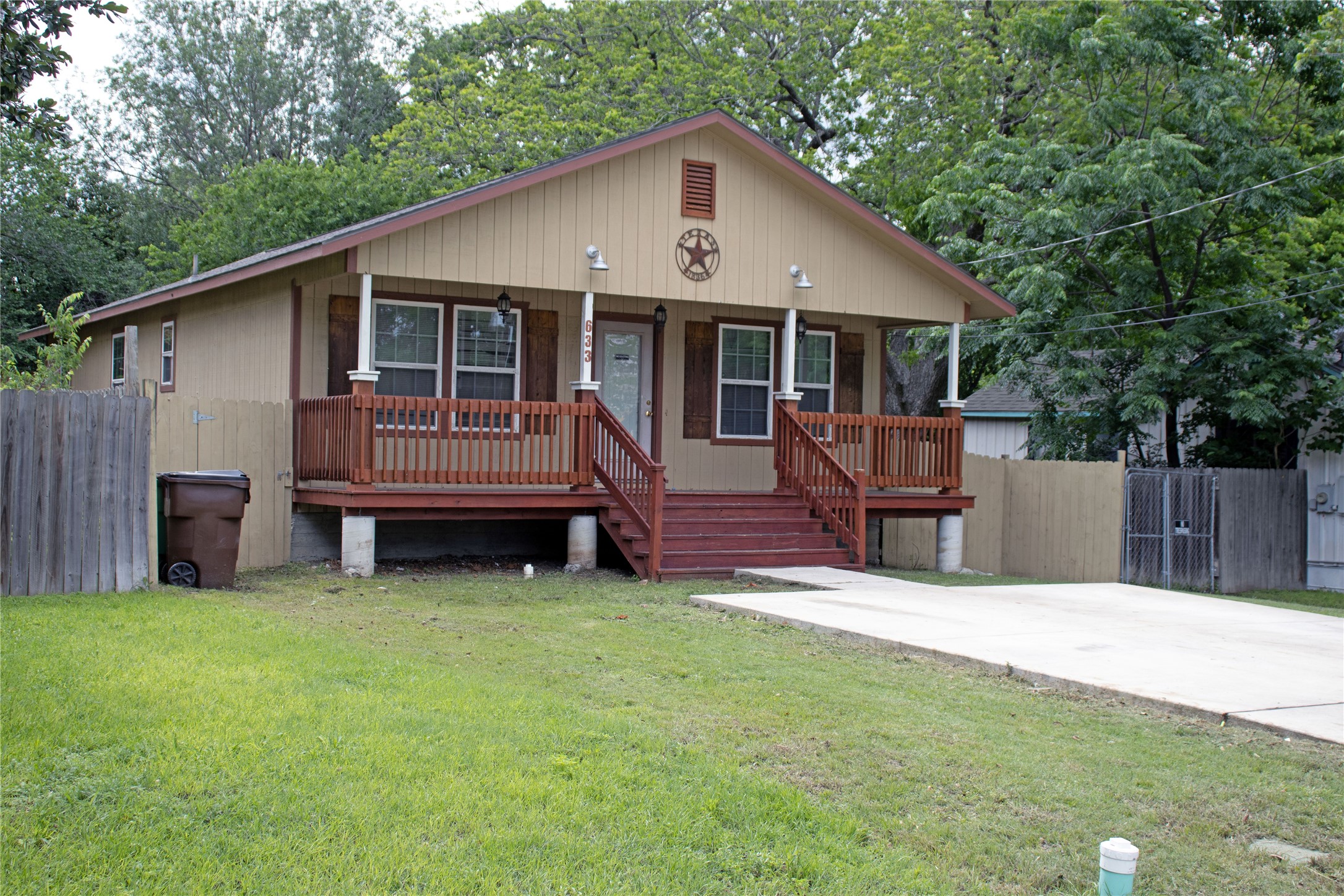 633 South Commerce Street Lockhart, TX 78644 - Photo 5 of 29 Front facade featuring a covered porch with dark wood railings and stairs, a light tan siding exterior, and a concrete driveway