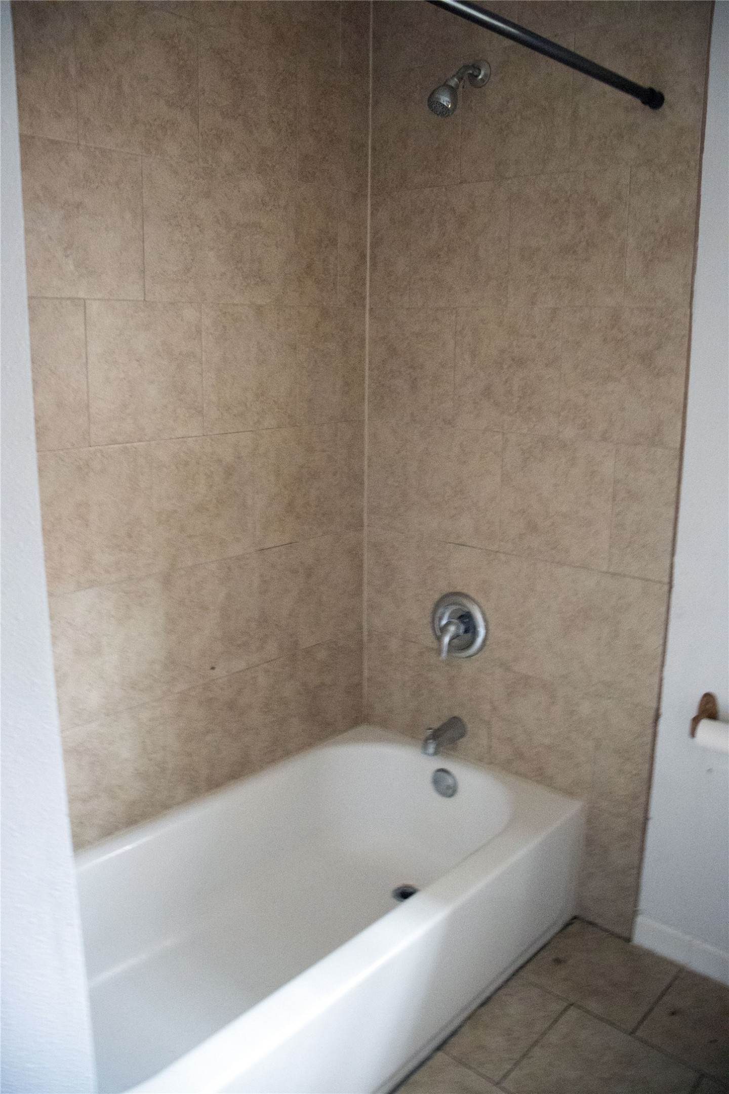 633 South Commerce Street Lockhart, TX 78644 - Photo 9 of 29 Bathtub and shower combination featuring neutral-toned wall tiles, a polished chrome shower head, and matching fixtures