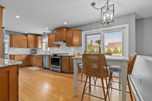 a kitchen with stainless steel appliances granite countertop a stove top oven a sink a dining table and chairs with wooden floor