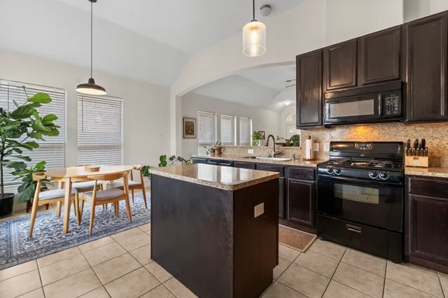 a kitchen with kitchen island granite countertop a stove top oven a sink a dining table and chairs