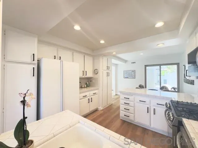 a kitchen with stainless steel appliances kitchen island granite countertop a refrigerator a sink dishwasher a dining table and chairs with wooden floor