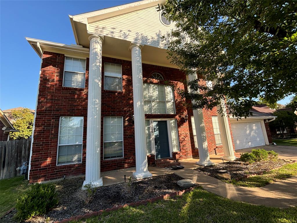 Neoclassical home with an attached garage, driveway, fence, and brick siding
