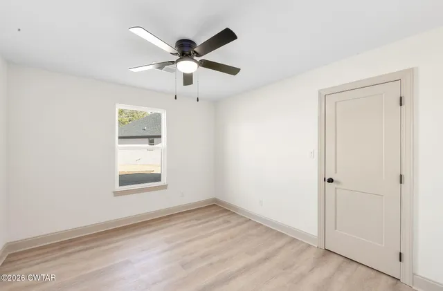 an empty room with wooden floor closet and windows