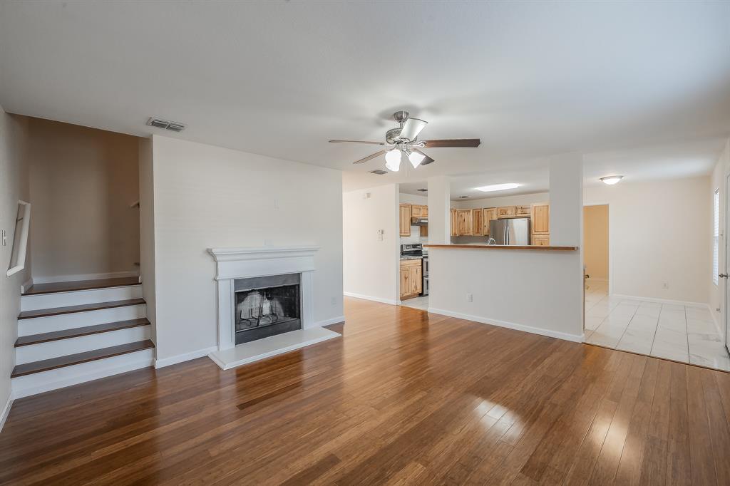 12109 Arbor Lake Road Rhome, TX 76078 - Photo 12 of 33 Unfurnished living room featuring a fireplace with raised hearth, light wood-type flooring, stairs, and a ceiling fan
