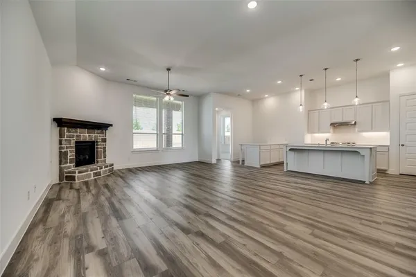 a view of an empty room and kitchen with fireplace wooden floor
