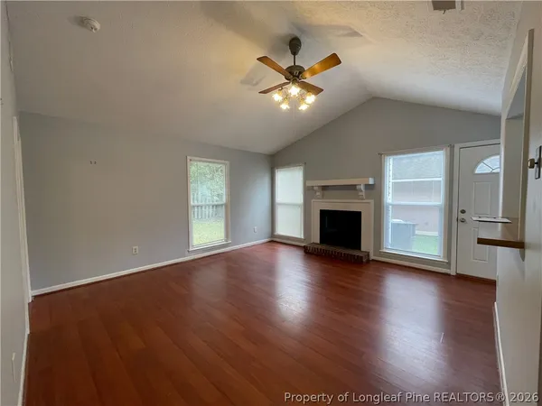 an empty room with wooden floor fireplace and windows